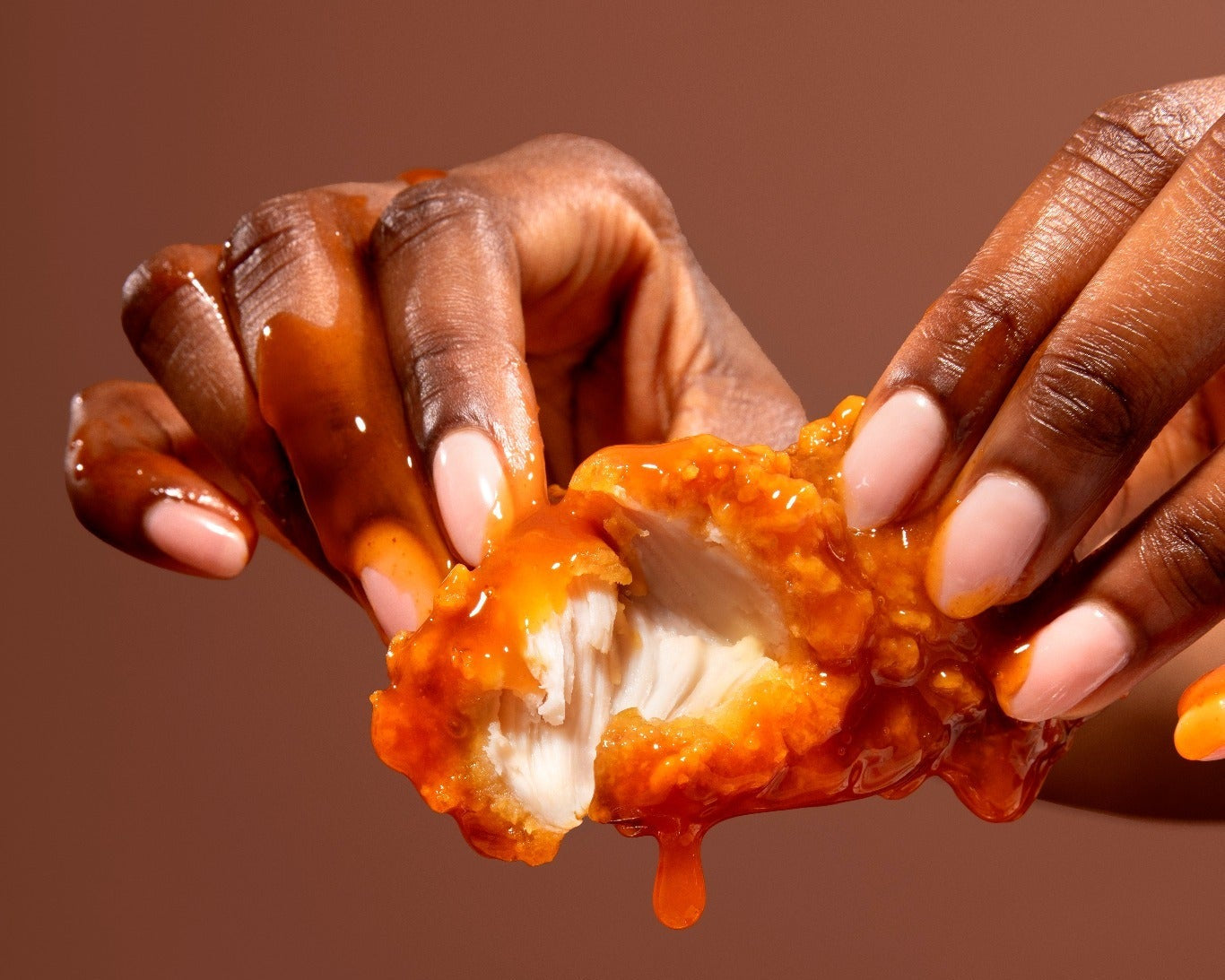 Hands holding a piece of buffalo chicken against a brown background shot by shaded the studio