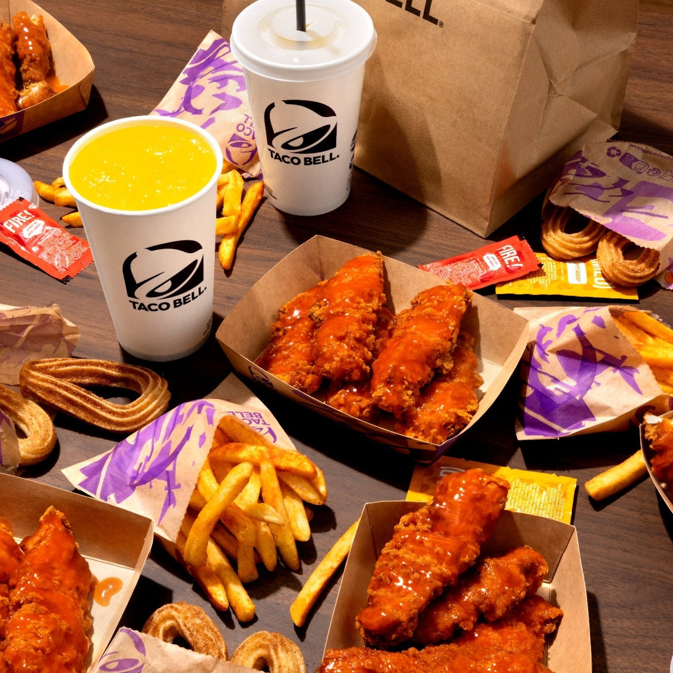 Person holding a box of chicken wings with one wing raised, against a brown background 