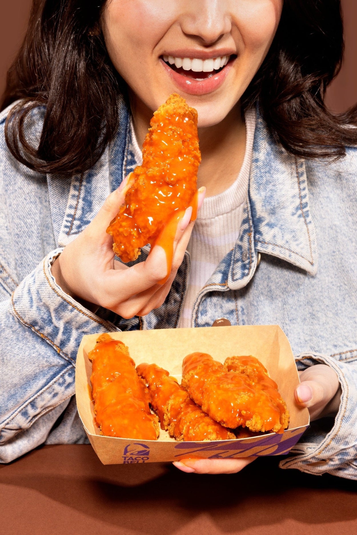 Person holding a box of chicken wings with one wing raised, against a brown background shot by Shaded The Studio